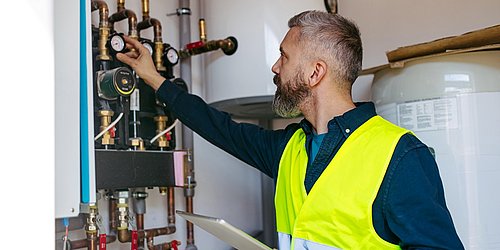 Handwerker stellt Heizungsanlage im Heizungskeller ein – digitales Heizungsmonitoring für mehr Effizienz.
