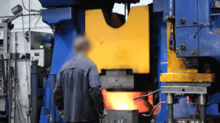 Ein Mitarbeiter steht vor einem glühenden Hochofen und überwacht die Produktion.