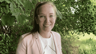 Porträt von Janika Gabriel vor einer grünen Hecke.