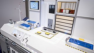 Detailansicht auf e2d2 – der KMU-Demonstrator: Auf einer Plattform wird ein beispielhafter Betrieb dargestellt mit Industrieanlagen, externer Energieversorgung und Dashboard.