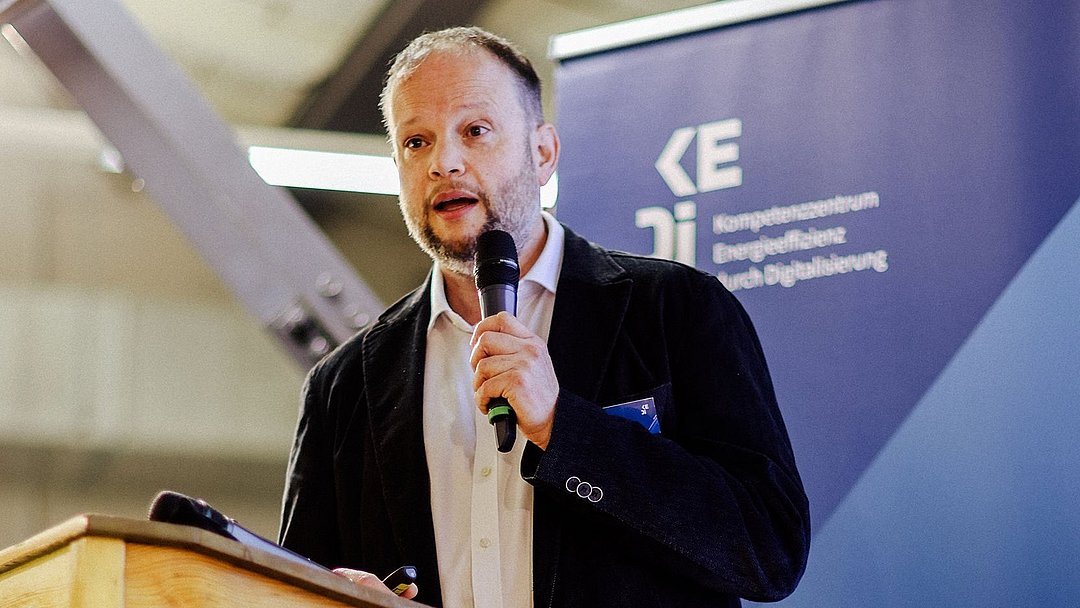 Steffen Grau steht auf der Bühne mit einem Mikrofon in der Hand und hält seinen Vortrag.
