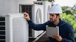 Ein Handwerker überprüft eine Wärmepumpe. Diese ist außen an einer Hauswand installiert.