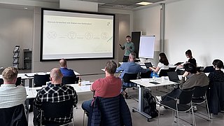 Die Teilnehmenden des Workshops sitzen in einem Raum und hören dem Vortrag zu.