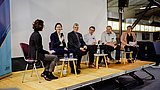 Die Teilnehmenden der Podiumsdiskussion sitzen auf der Bühne und unterhalten sich.