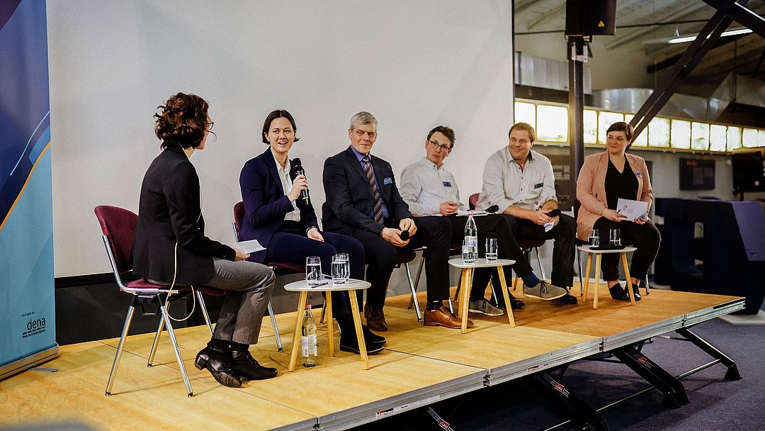 Die Teilnehmenden der Podiumsdiskussion sitzen auf der Bühne und unterhalten sich.