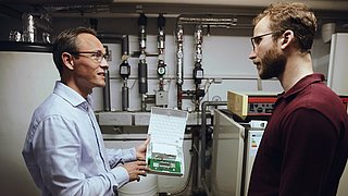 Tim Ulrich erklärt im Heizungskeller Thomas Koutalidis die Funktionsweise des Gateways. 