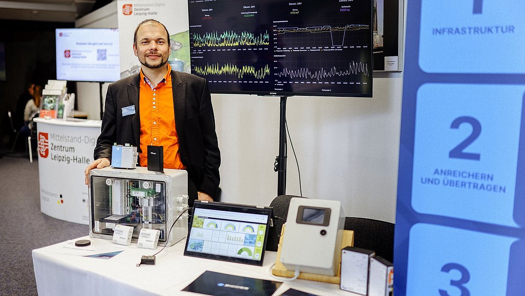 Eine Person steht an einem Informationsstand und lächelt in die Kamera.