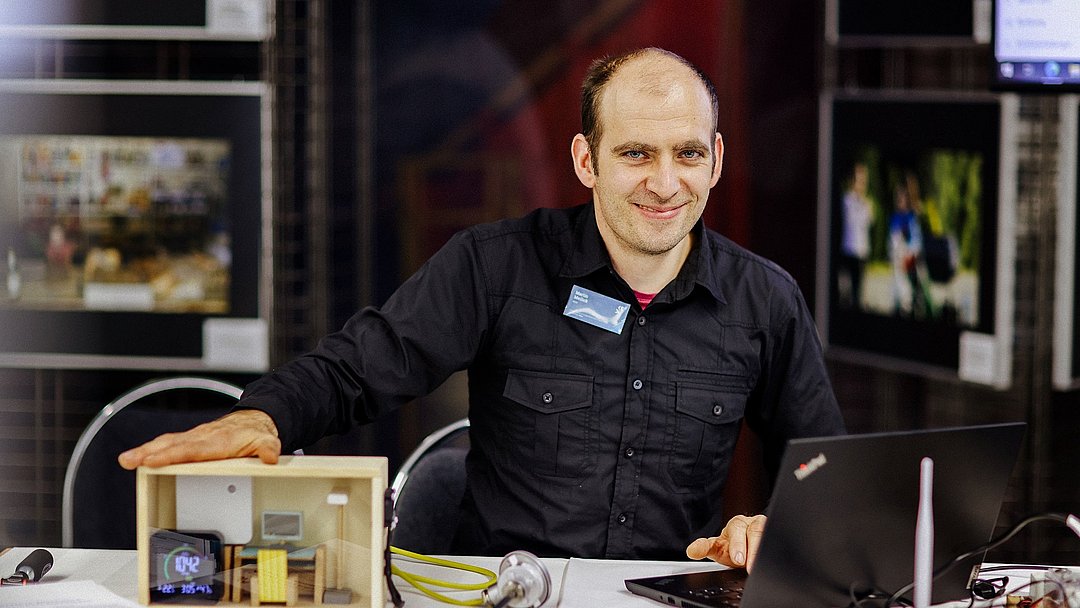 Martin Meilick sitzt an einem Tisch und präsentiert den Demonstrator.