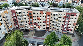 Vogelperspektive auf einen Wohnblock. Auf dem Dach sind zahlreiche PV-Anlagen. Im Hintergrund stehen weitere Wohnhäuser.
