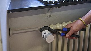 Eine Person befestigt mit einer Rohrzange das neue Ventil an einer Heizung.