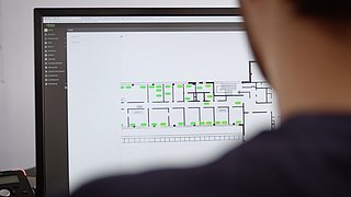 Eine Person sitzt vor einem Bildschirm. Auf dem Display ist ein Dashboard für die Steuerung der Heizungsanlage.