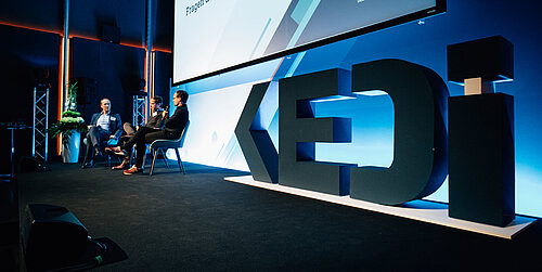 Ein Blick auf die Bühne der Eröffnung mit Mitarbeitenden und dem 3D-Logo des KEDi