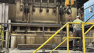 Ein Mitarbeiter steht vor dem Herdwagen-Durchschubofen und bereitet eine Stahlbramme zur Bearbeitung vor.