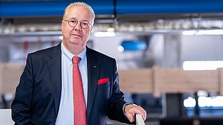 Thomas Kübler steht im Anzug in einer Produktionshalle.