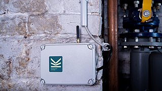 Auf dem Bild ist die weiße Steuerbox, die an einer weißen Backsteinwand im Heizungskeller befestig ist zu sehen.