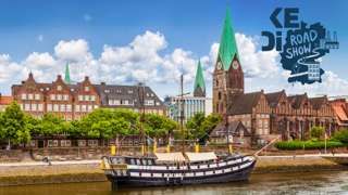 Ein Segelschiff liegt an einer Promenade an. Im Hintergrund sind historische Gebäude der Stadt Bremen.
