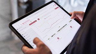 Eine Person hält ein Tablet in der Hand. Auf dem Display sieht man ein Dashboard mit Verbrauchswerten..