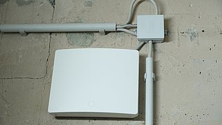 Ein Gateway hängt an einer Kellerwand. An den Seiten sind Kabelschächte montiert.
